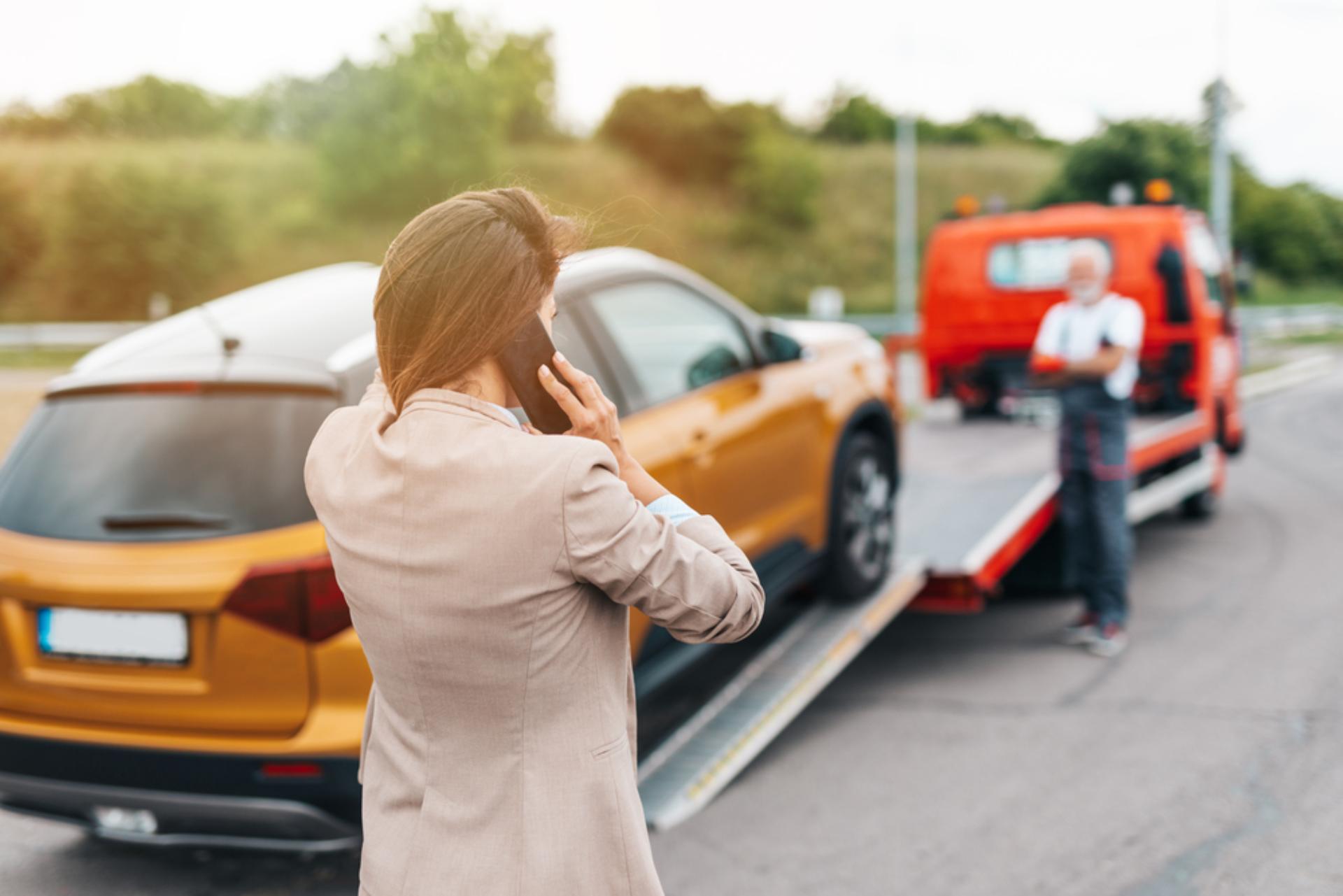 A woman pictured with her back to the viewer, on the phone as her vehicle is towed